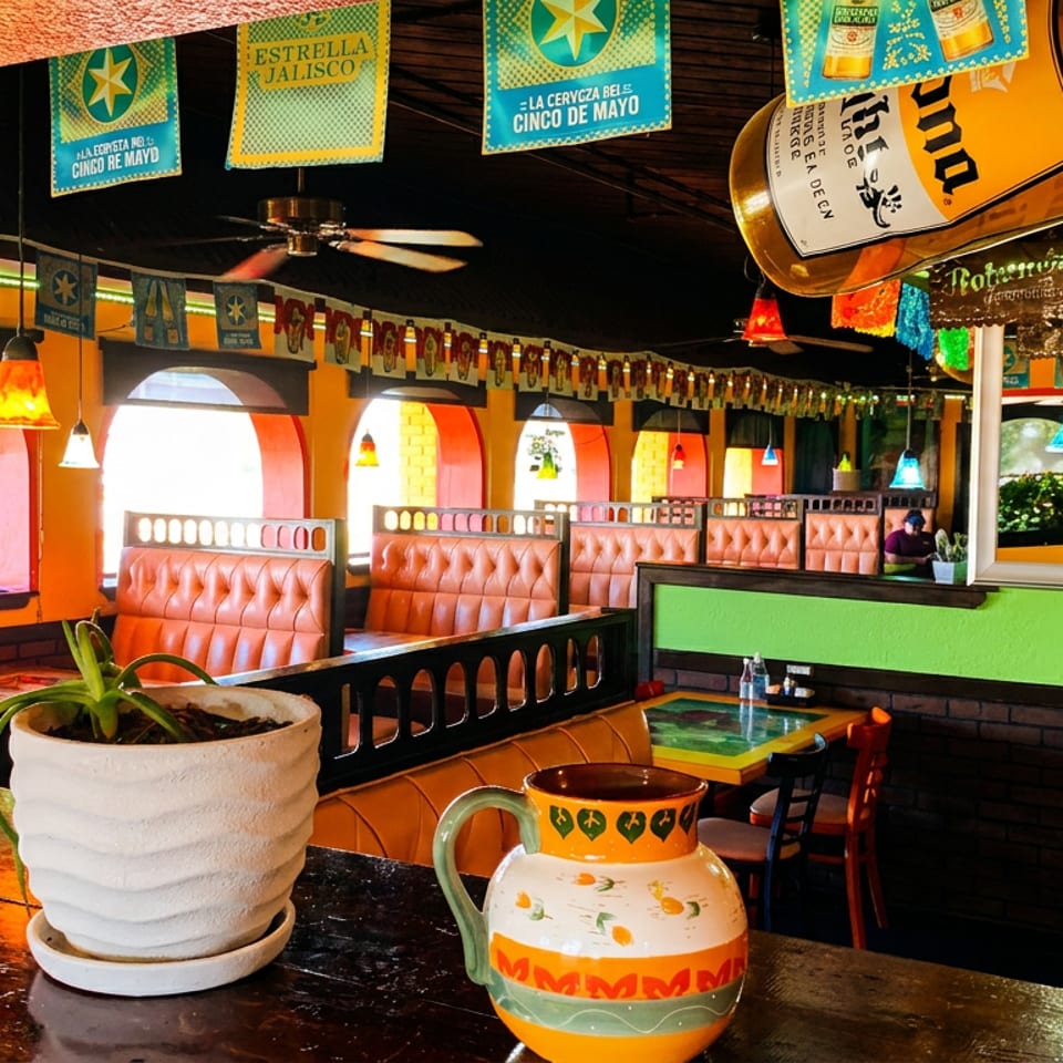Vibrant Mexican restaurant interior with orange booths, colorful banners, and decorative lighting.