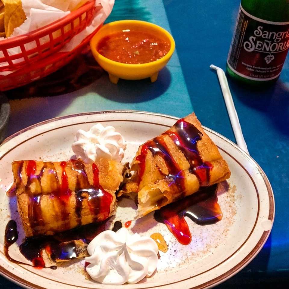 Fried dessert chimichangas with whipped cream, chocolate, and strawberry syrup, alongside chips and salsa.