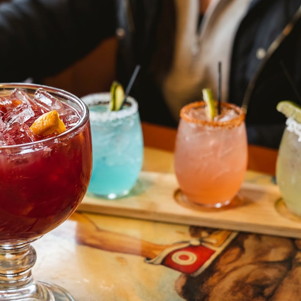 A large red sangria with fruit and ice, alongside a flight of colorful margaritas.